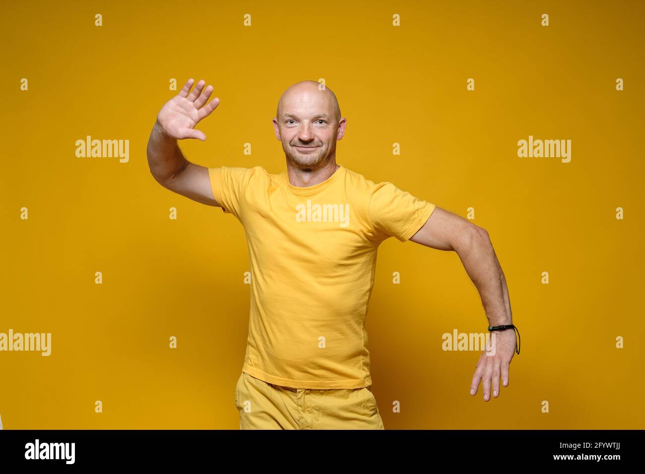 Funny bald, Caucasian man in yellow clothes stands with a bizarre pose and looks at the camera. Bright background. Stock Photo