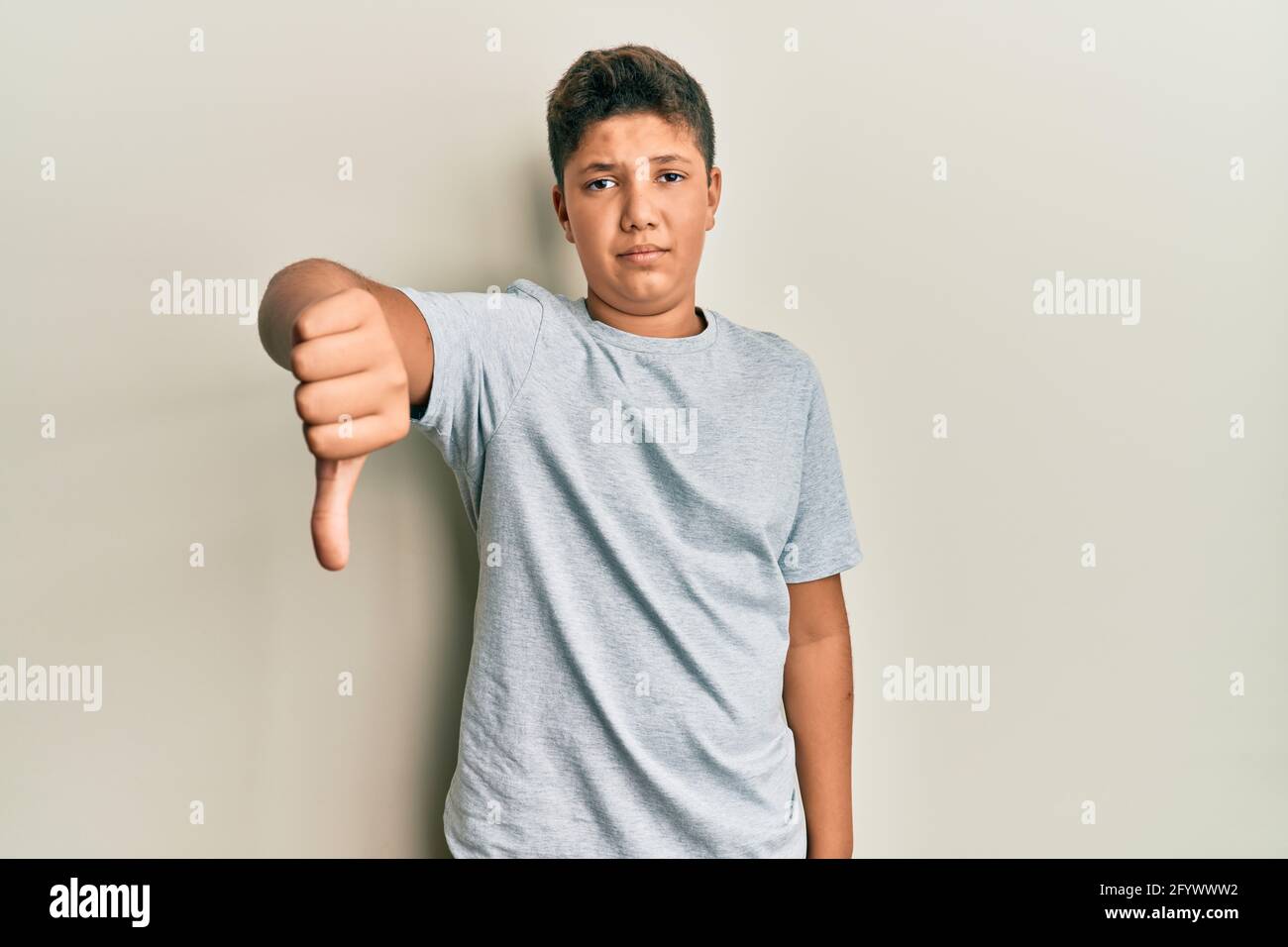 Teenager hispanic boy wearing casual grey t shirt looking unhappy and ...