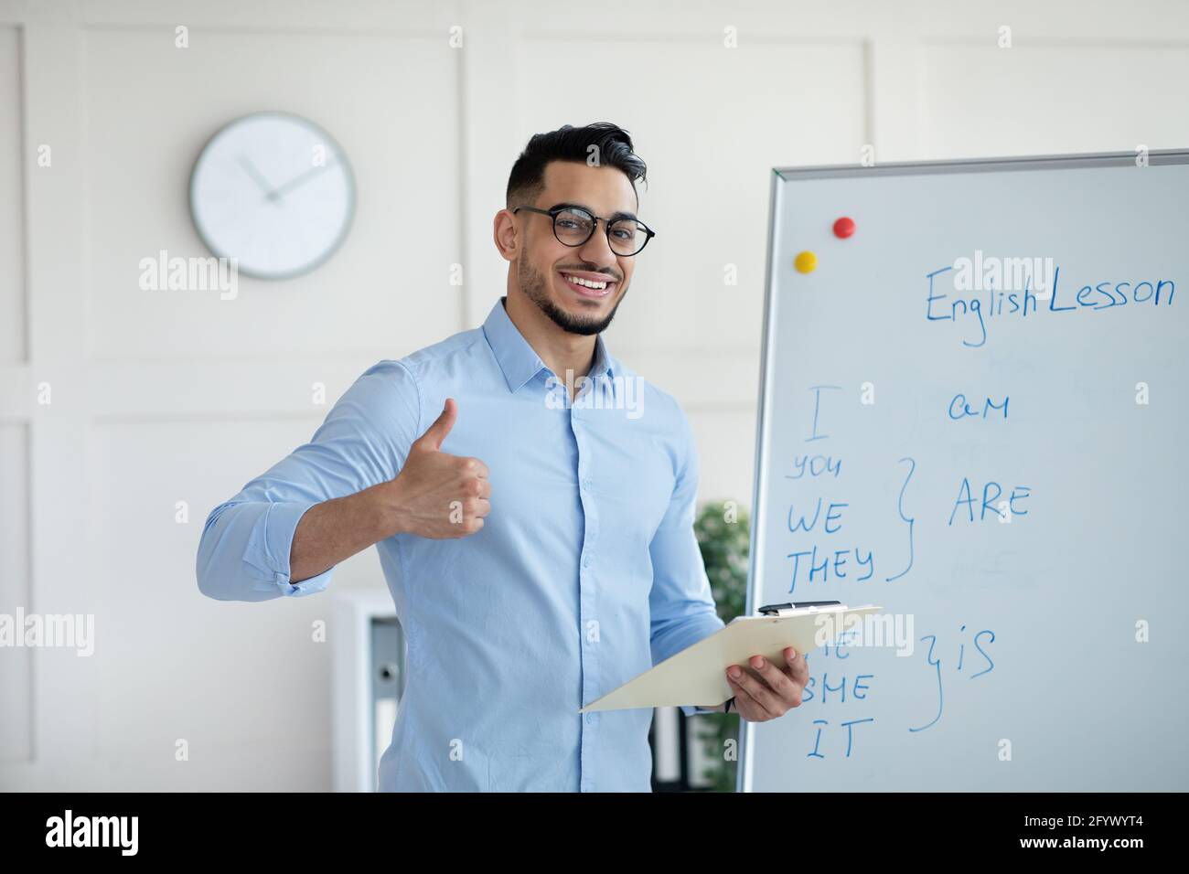 Arab male teacher showing thumb up near blackboard, teaching English on web, recommending online foreign language school Stock Photo