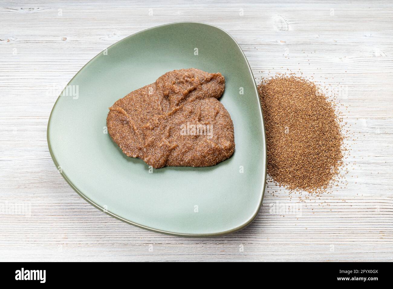 teff grains and boiled porridge on green plate on wooden table Stock Photo
