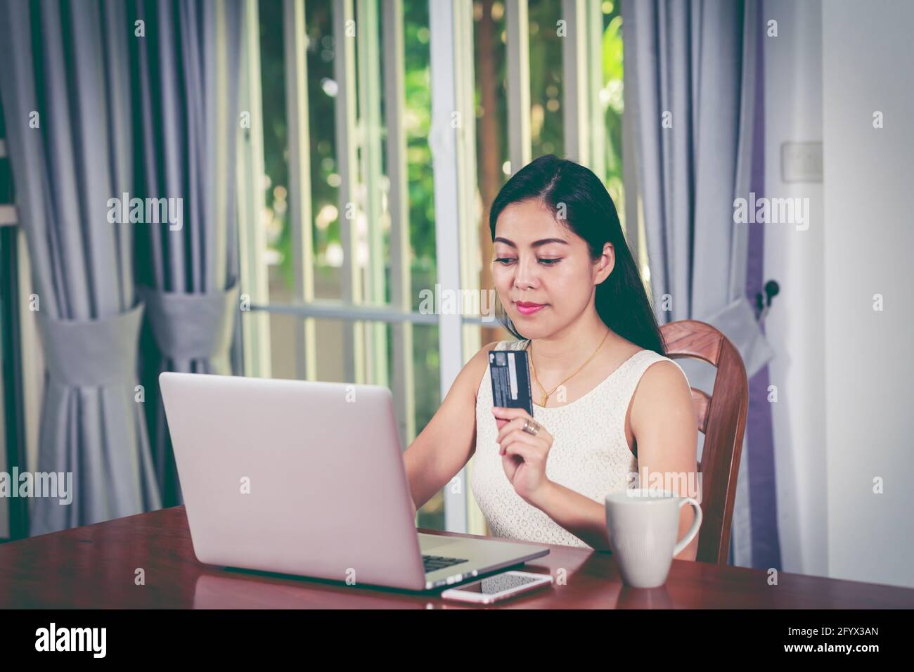 Beautiful asian woman holding credit card and making order at home. Young adult using laptop computer for shopping on internet. Online shopping concep Stock Photo