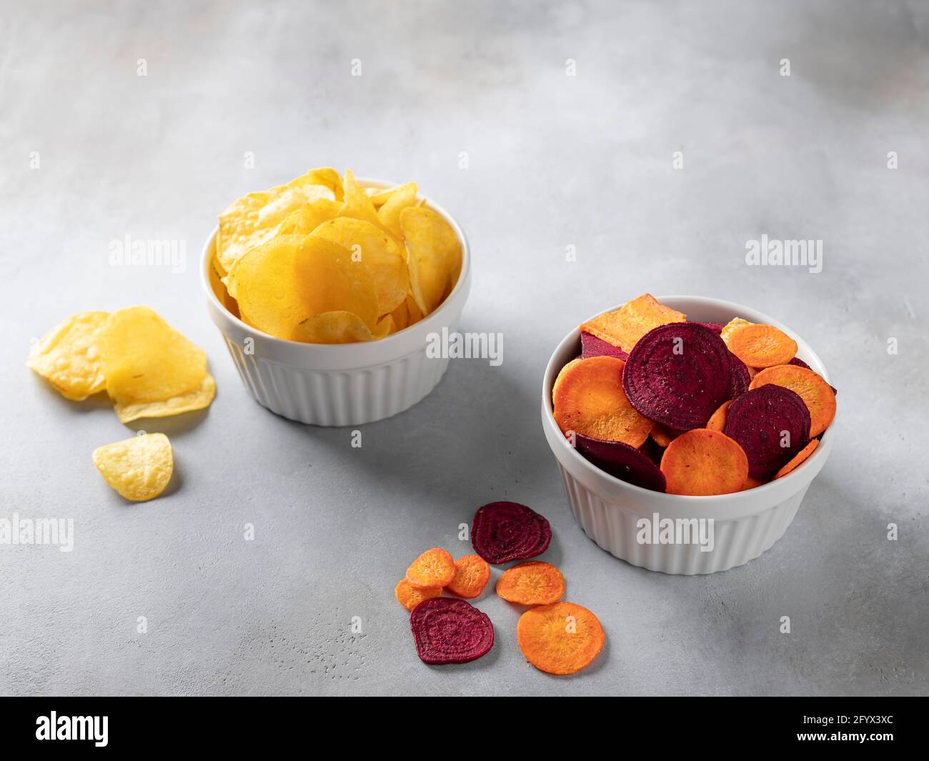 tasty potato, carrot, beet chips in bowls on gray background. vegan alternative food. horizontal image. copy space. Stock Photo