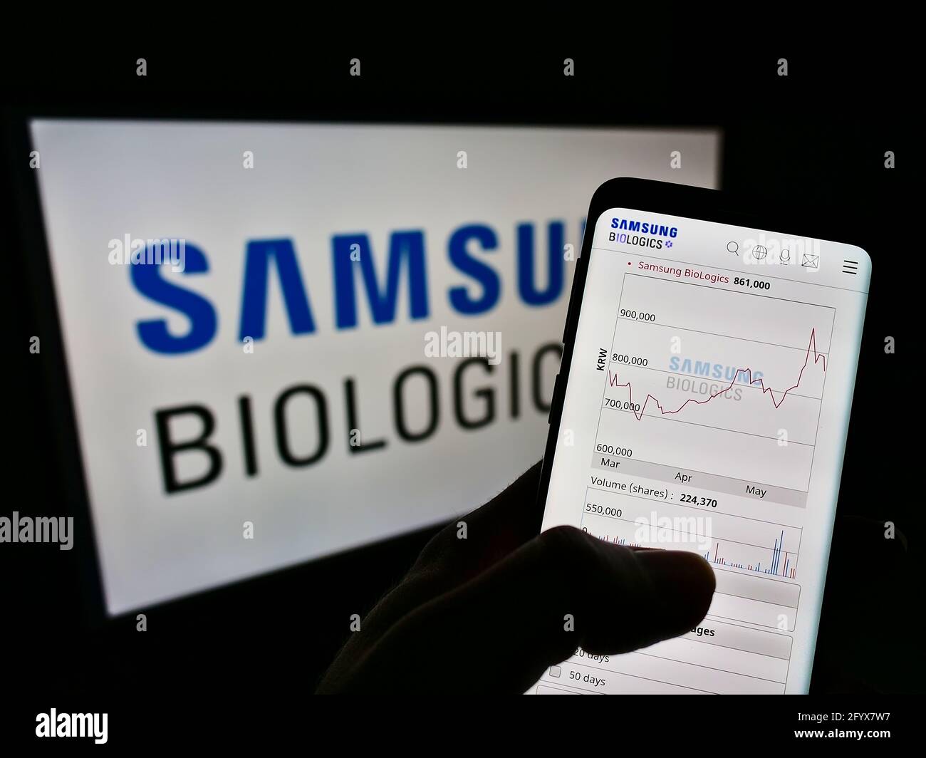 Person holding cellphone with webpage of biotechnology company Samsung Biologics Co Ltd on screen in front of logo. Focus on center of phone display. Stock Photo