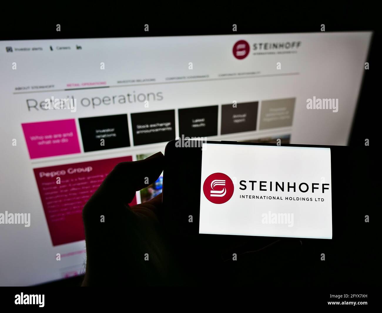 Person holding mobile phone with logo of retail company Steinhoff International Holdings N.V. on screen in front of webpage. Focus on phone display. Stock Photo