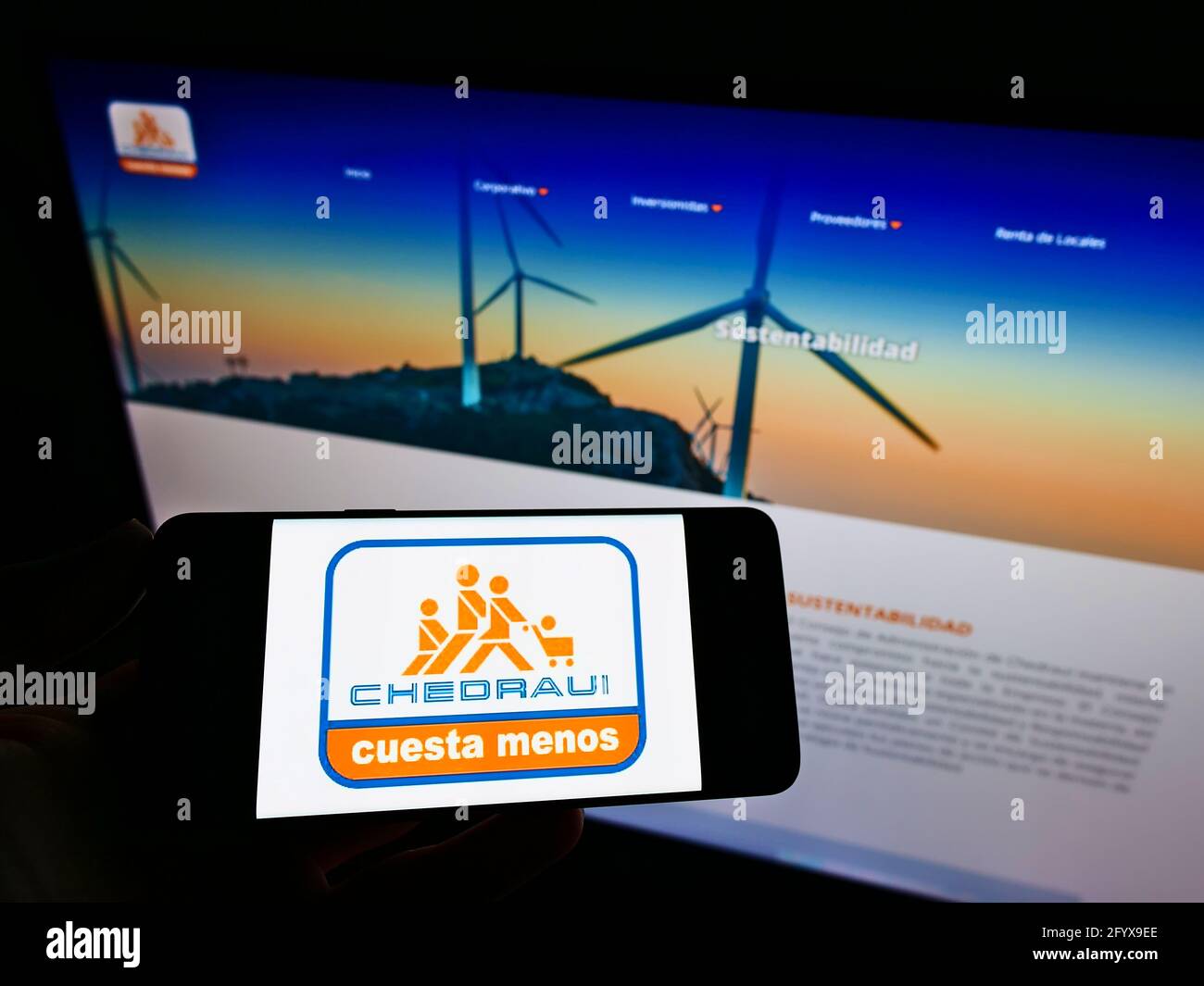 Person holding mobile phone with logo of Mexican Grupo Comercial Chedraui S.A.B. de C.V. on screen in front of web page. Focus on phone display. Stock Photo