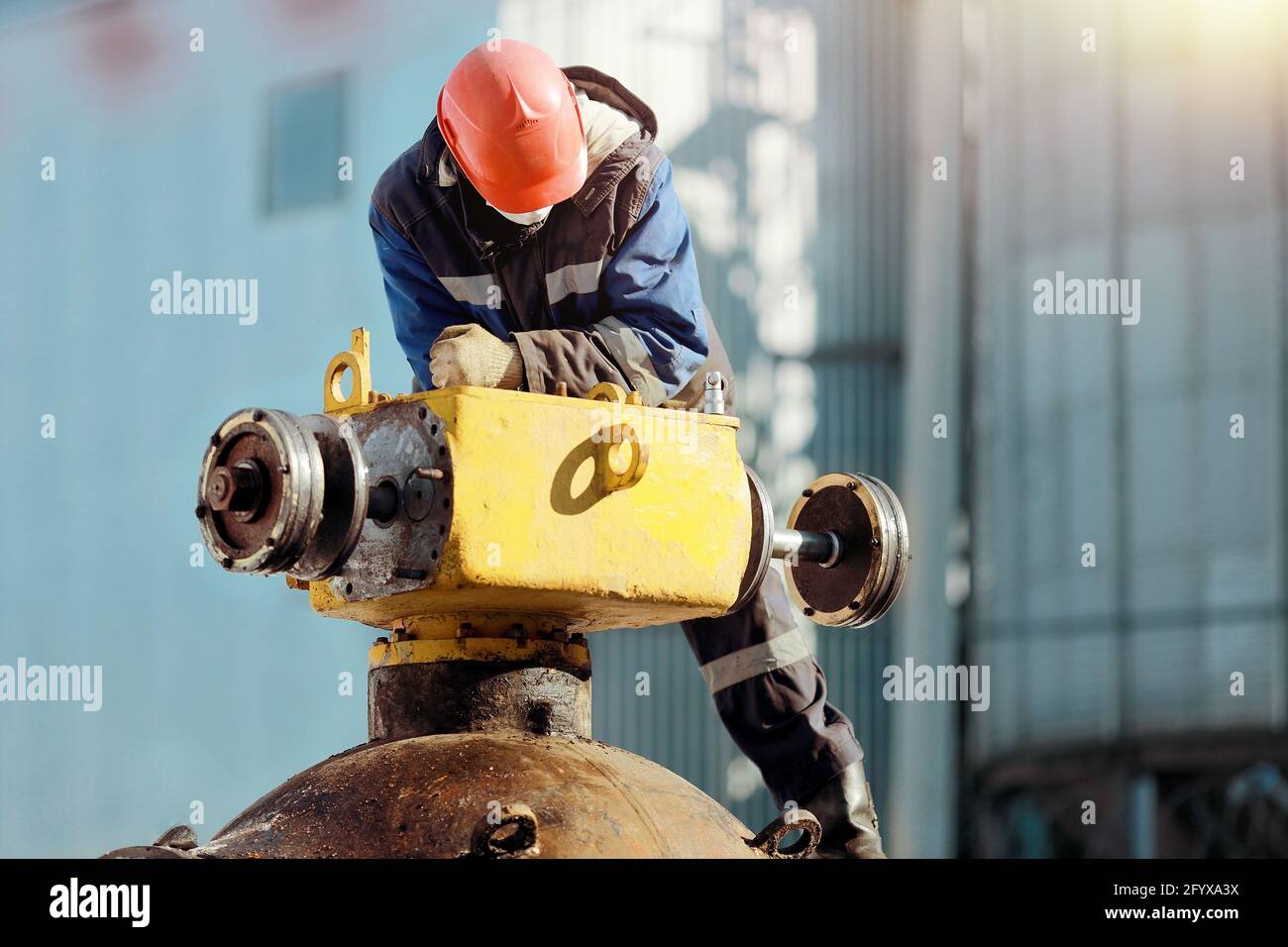 A man in work clothes and a hard hat works with gas equipment outdoors in winter. Repair of the linear crane of the main gas pipeline. Stock Photo