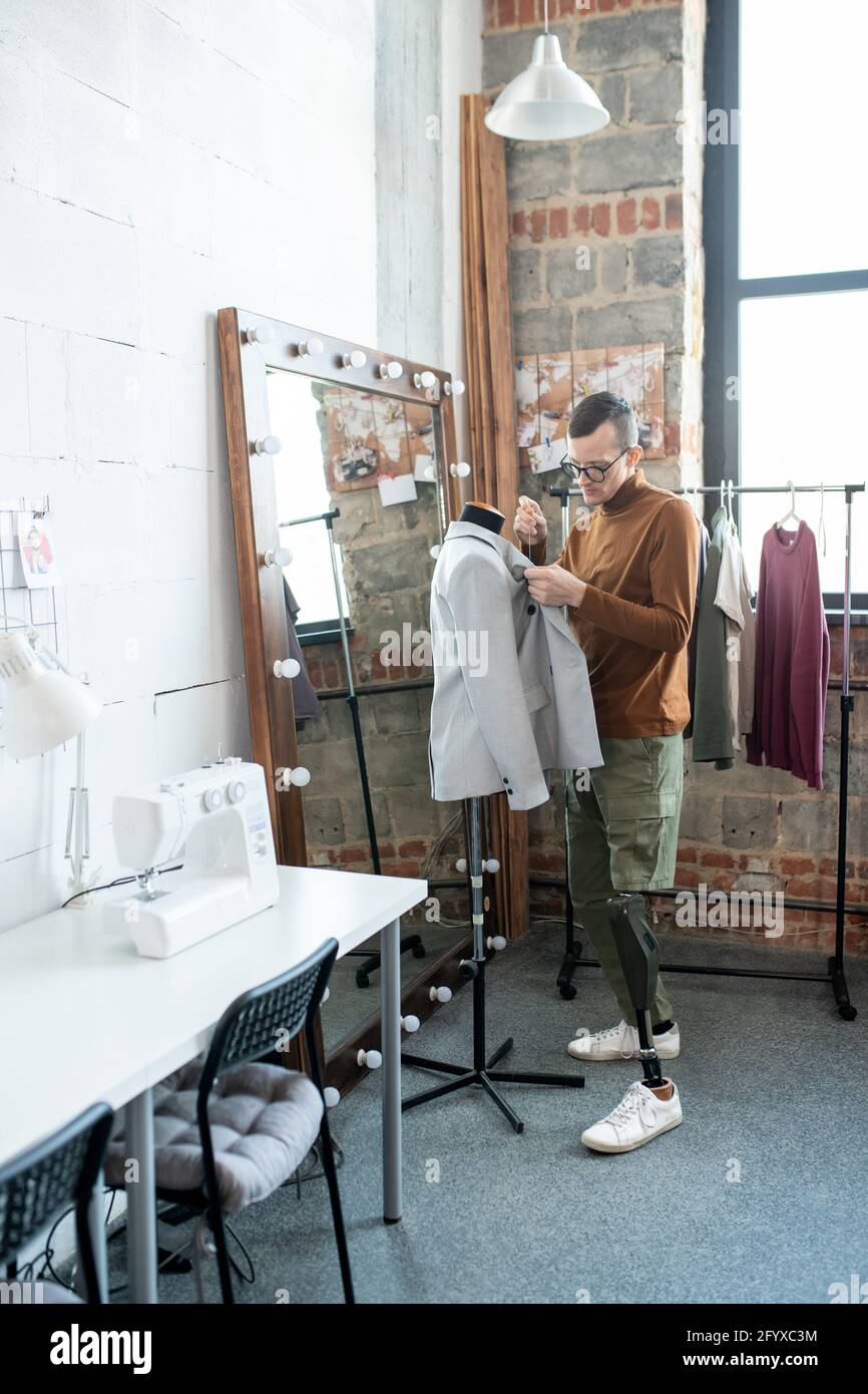 Disable man with leg prosthesis working over new jacket while standing by dummy Stock Photo
