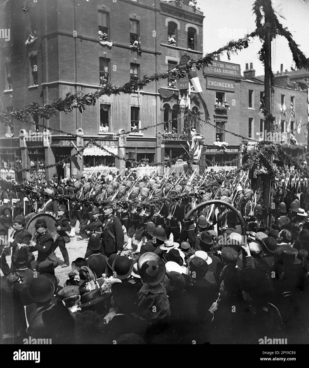 Onlookers watch as a marching band and colonial troop parade down the street during the procession for Queen Victoria's Diamond Jubilee, London, England, June 22, 1897. (Photo by Burton Holmes) Stock Photo