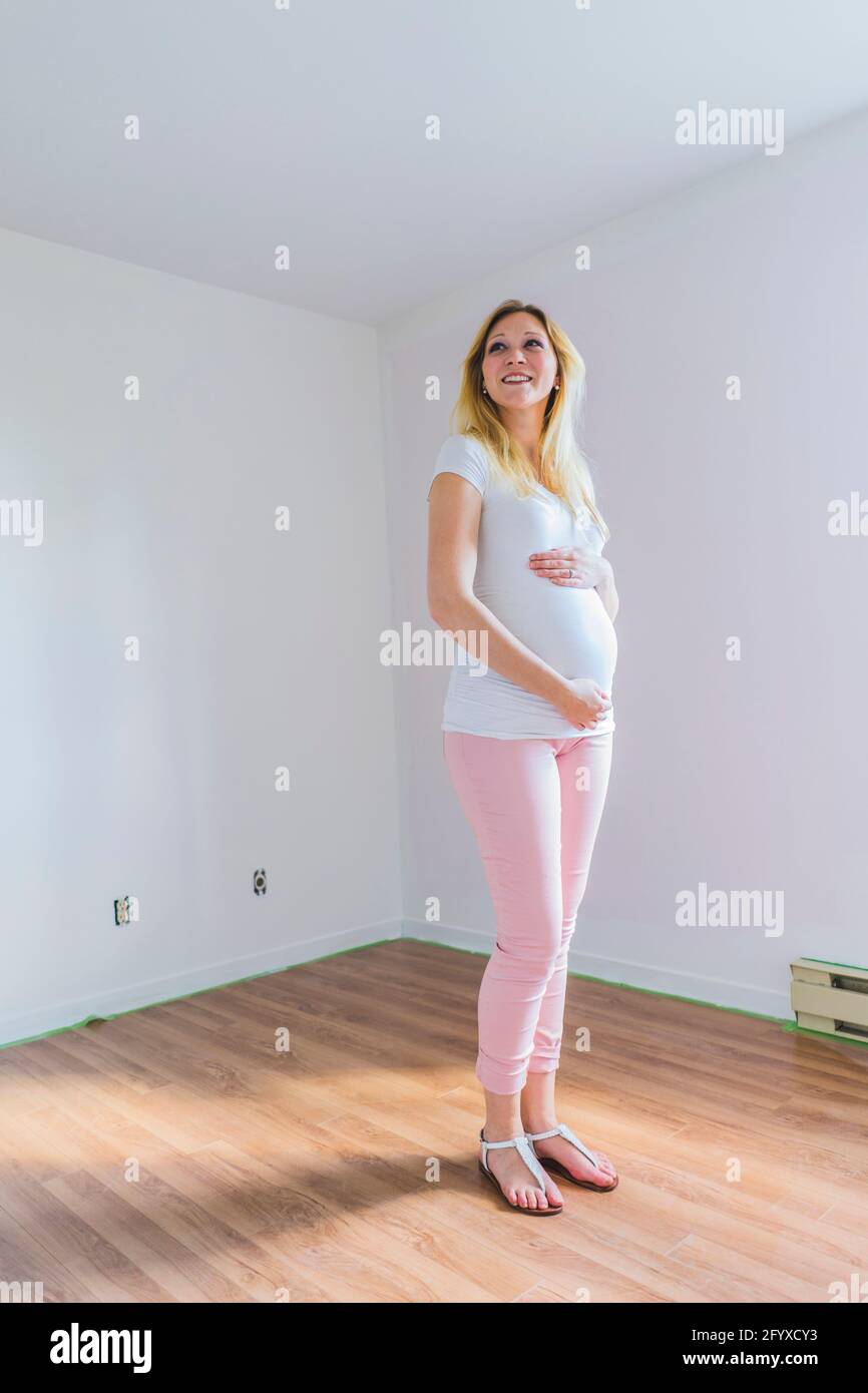 Beautiful blond pregnant woman standing in newly painted room during