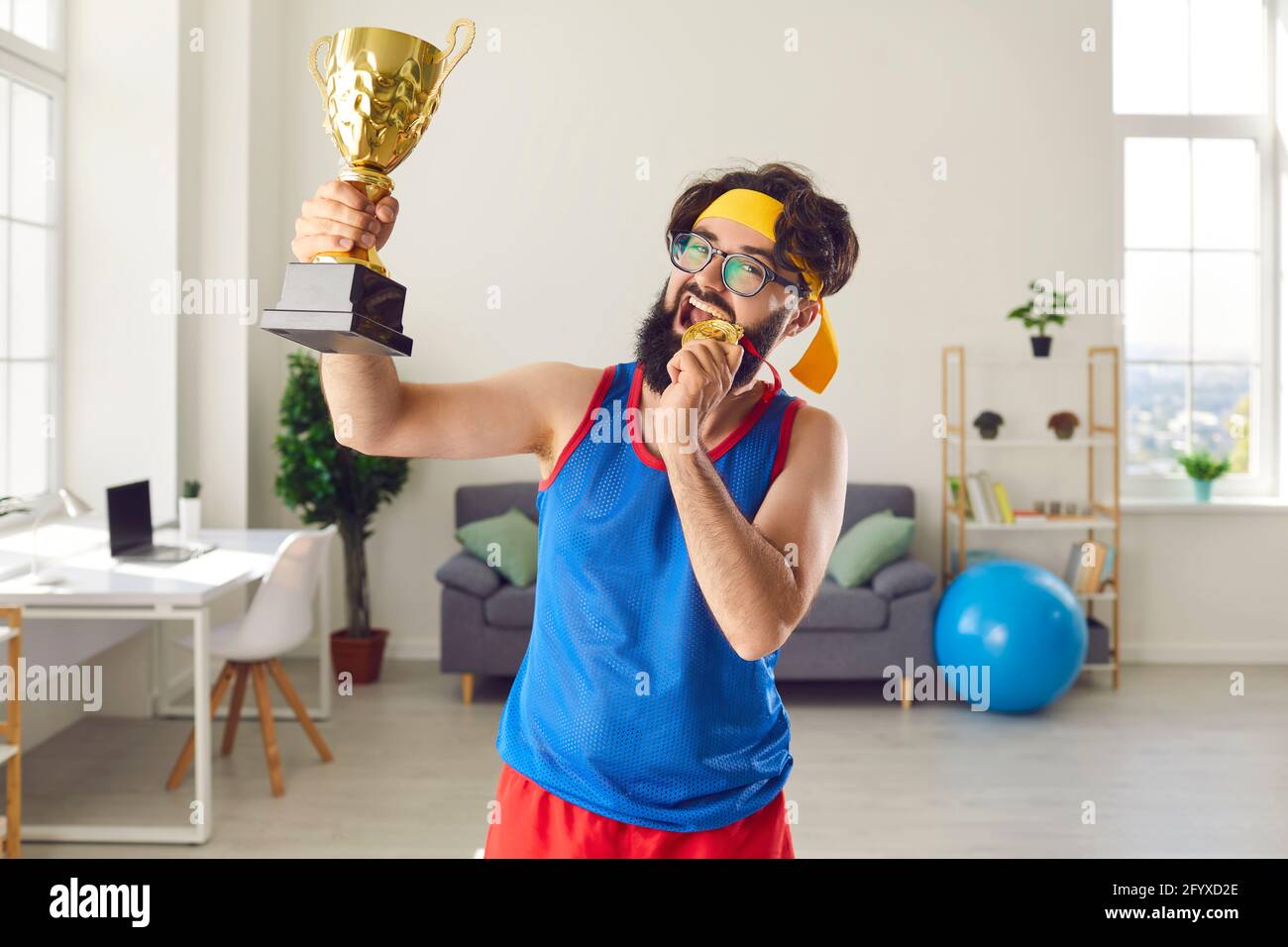 Happy funny man athlete biting golden medal and holding first prize trophy Stock Photo
