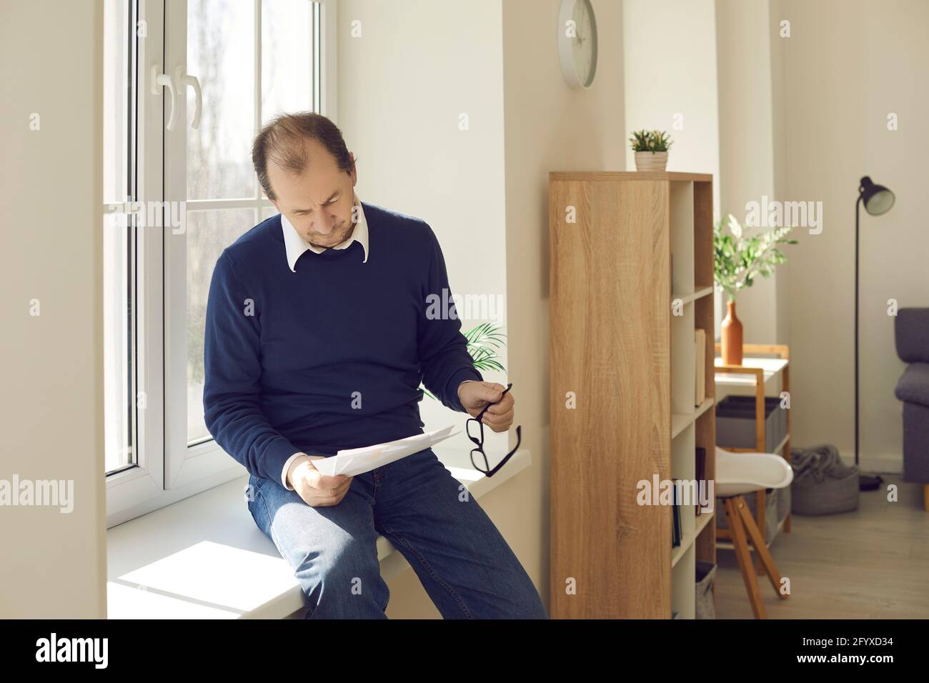 Mature businessman working with paper sitting on windowsill in home office Stock Photo