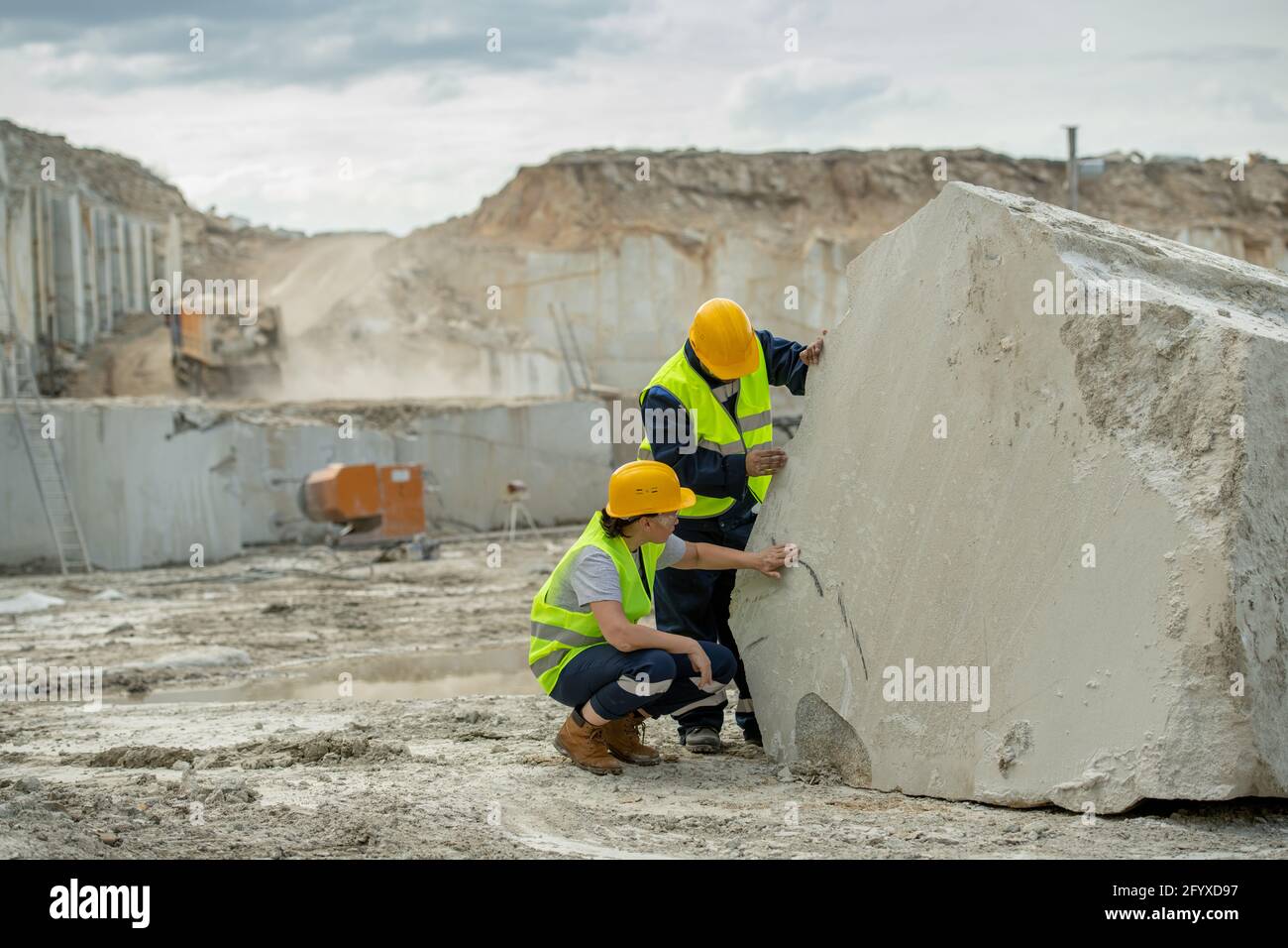 Two young builders in hardhats and uniform working by huge piece of concrete Stock Photo