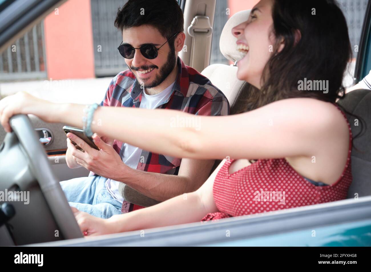 Two friends travel together driving a car, using the smartphone and laughing. Summer adventure. Stock Photo