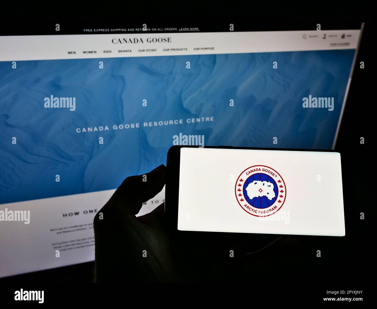 Person holding cellphone with logo of winter clothing company Canada Goose Holdings Inc. on screen in front of web page. Focus on phone display. Stock Photo