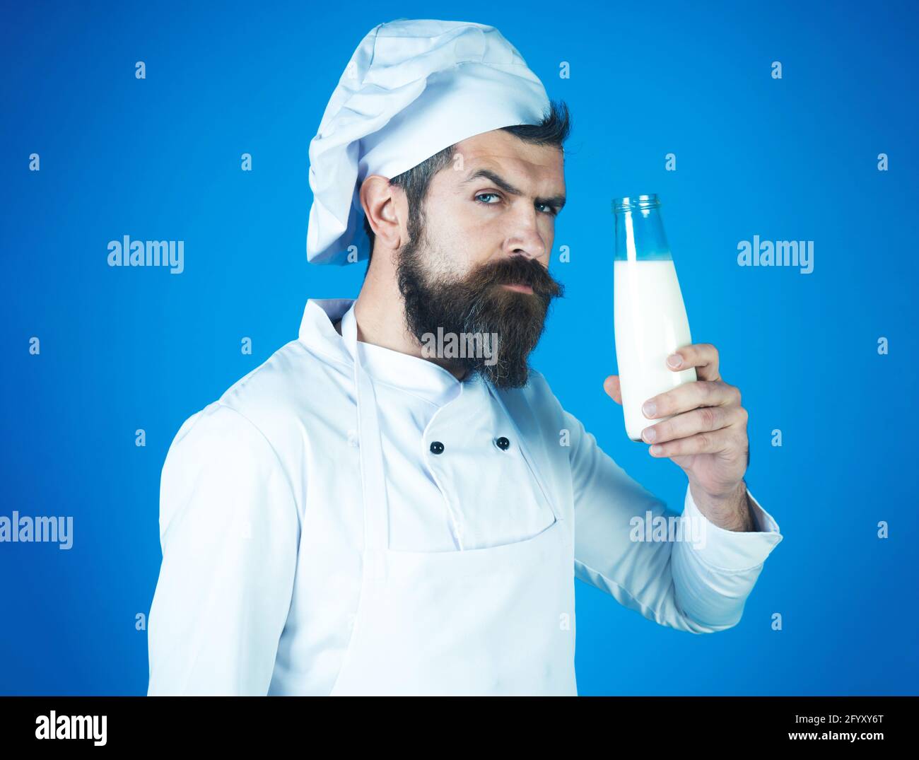 Bearded chef man in uniform with bottle of milk. Drinks, dairy farmer products, diet. Stock Photo