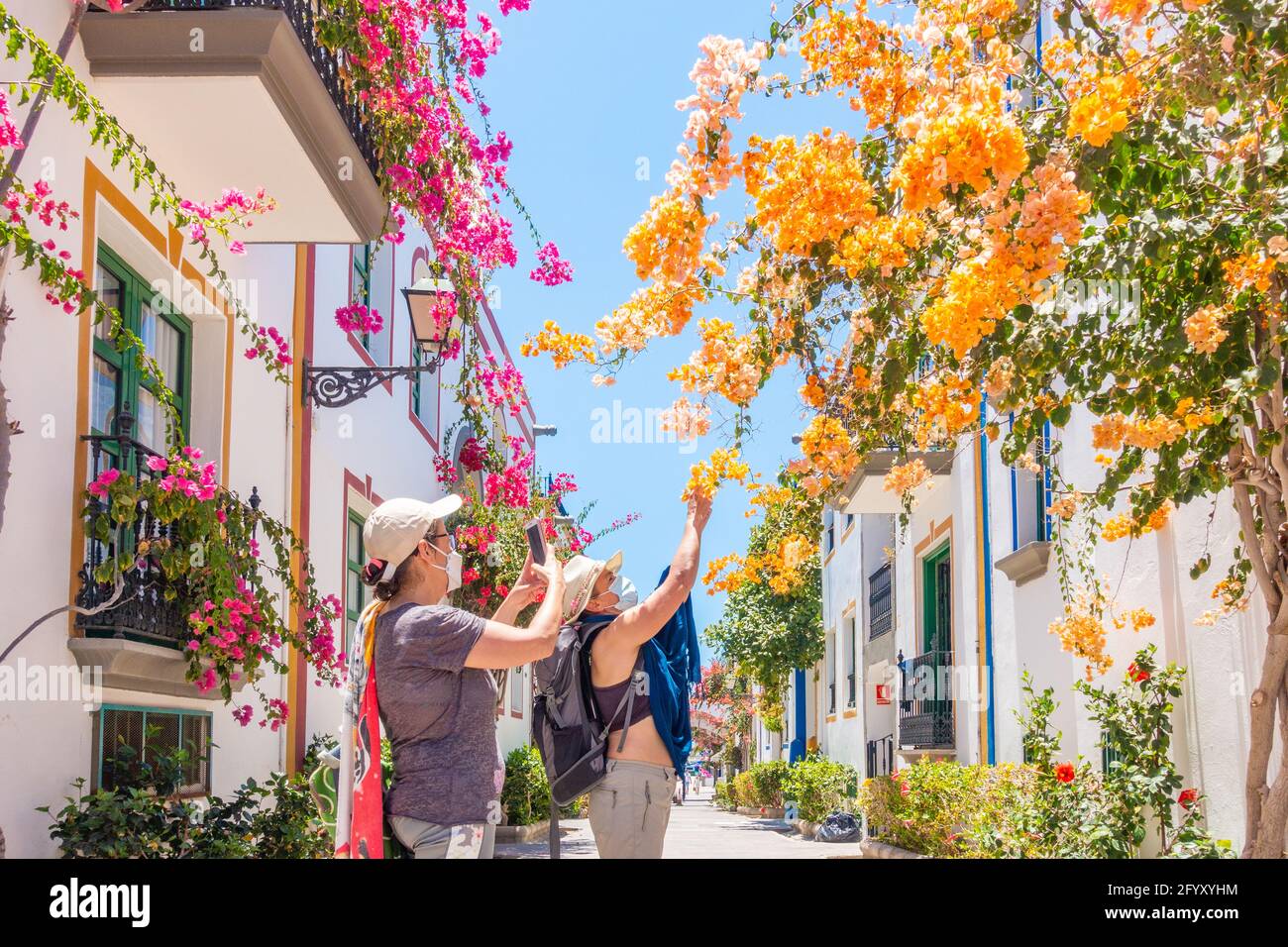 Tourists wearing Covid face masks taking photos of Bougainvillea at Puerto de Mogan, Gran