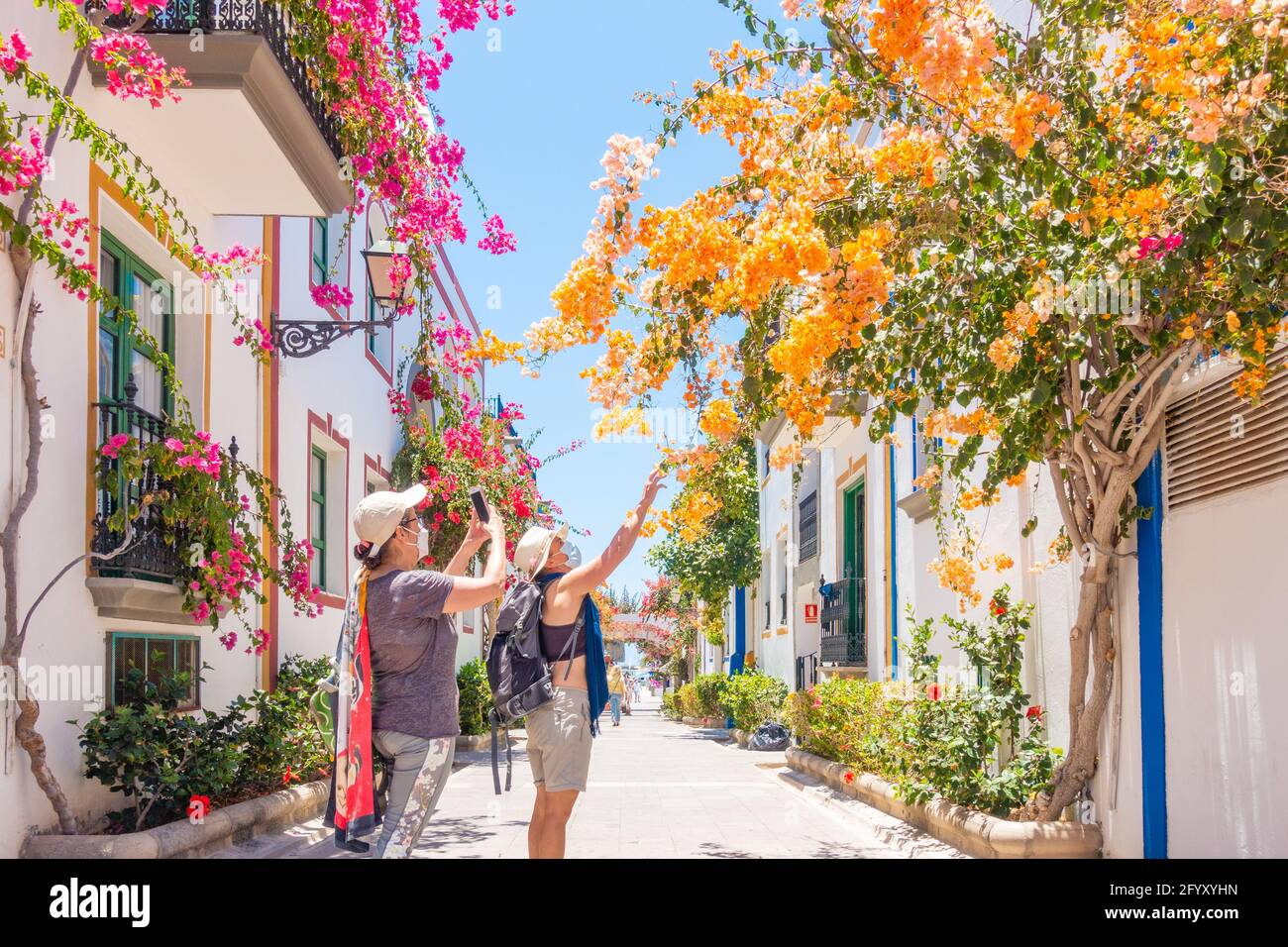 Tourists wearing Covid face masks taking photos of Bougainvillea at Puerto de Mogan, Gran