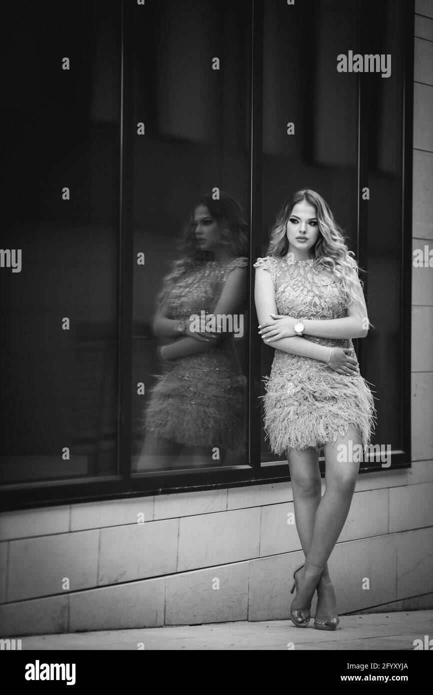 A vertical shot of a beautiful blonde female posing near glass building ...