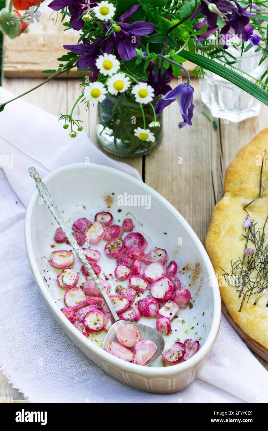 Focaccia with onions, baked radish and a bouquet of flowers on a wooden table. Stock Photo