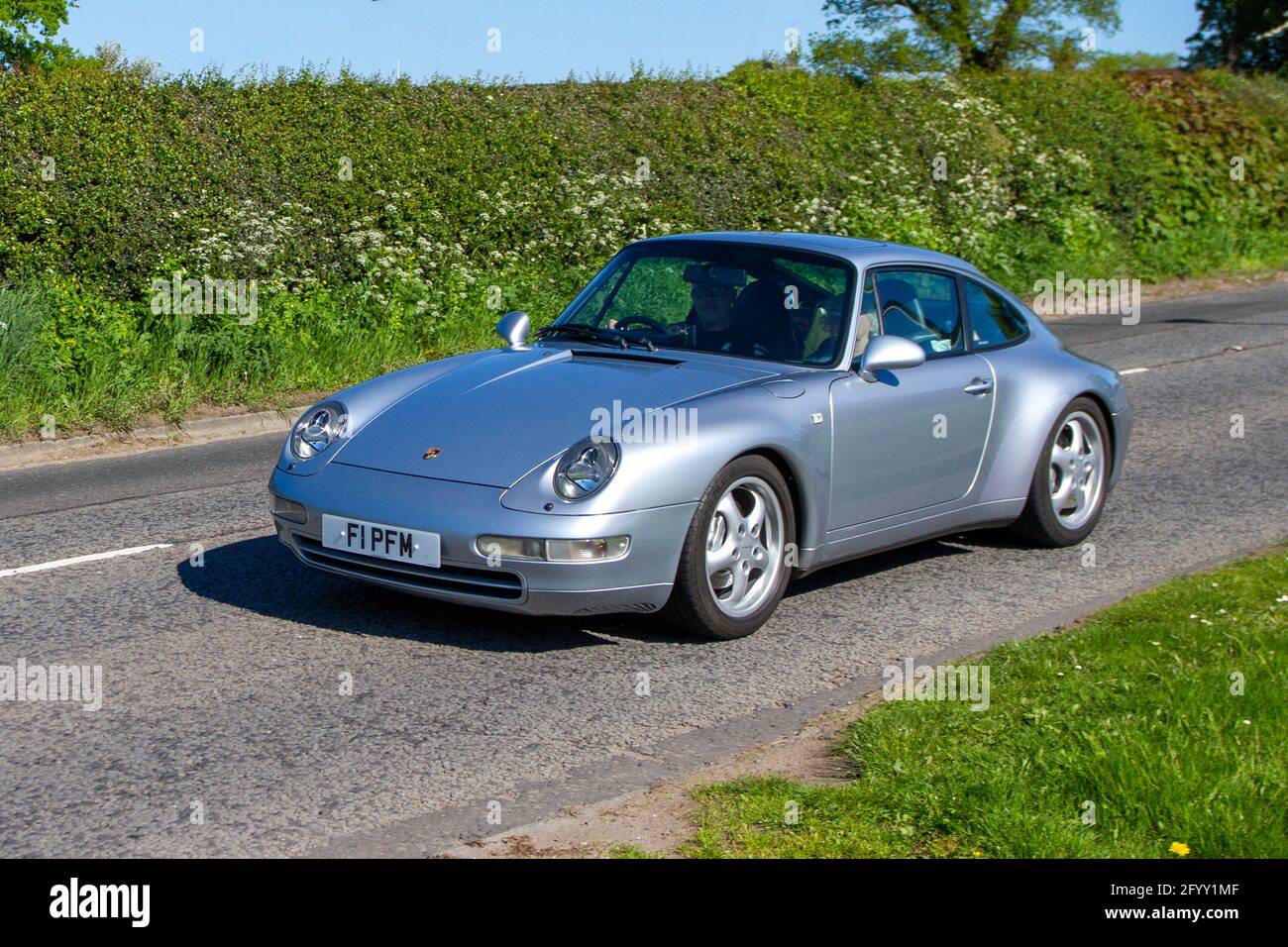 1996 90s silver Porsche 911 Carrera 4 two-door 2+2 high performance  rear-engined sports car ; Vehicular traffic, moving vehicles, cars, vehicle  driving en-route to Capesthorne Hall classic May car show, Cheshire, UK