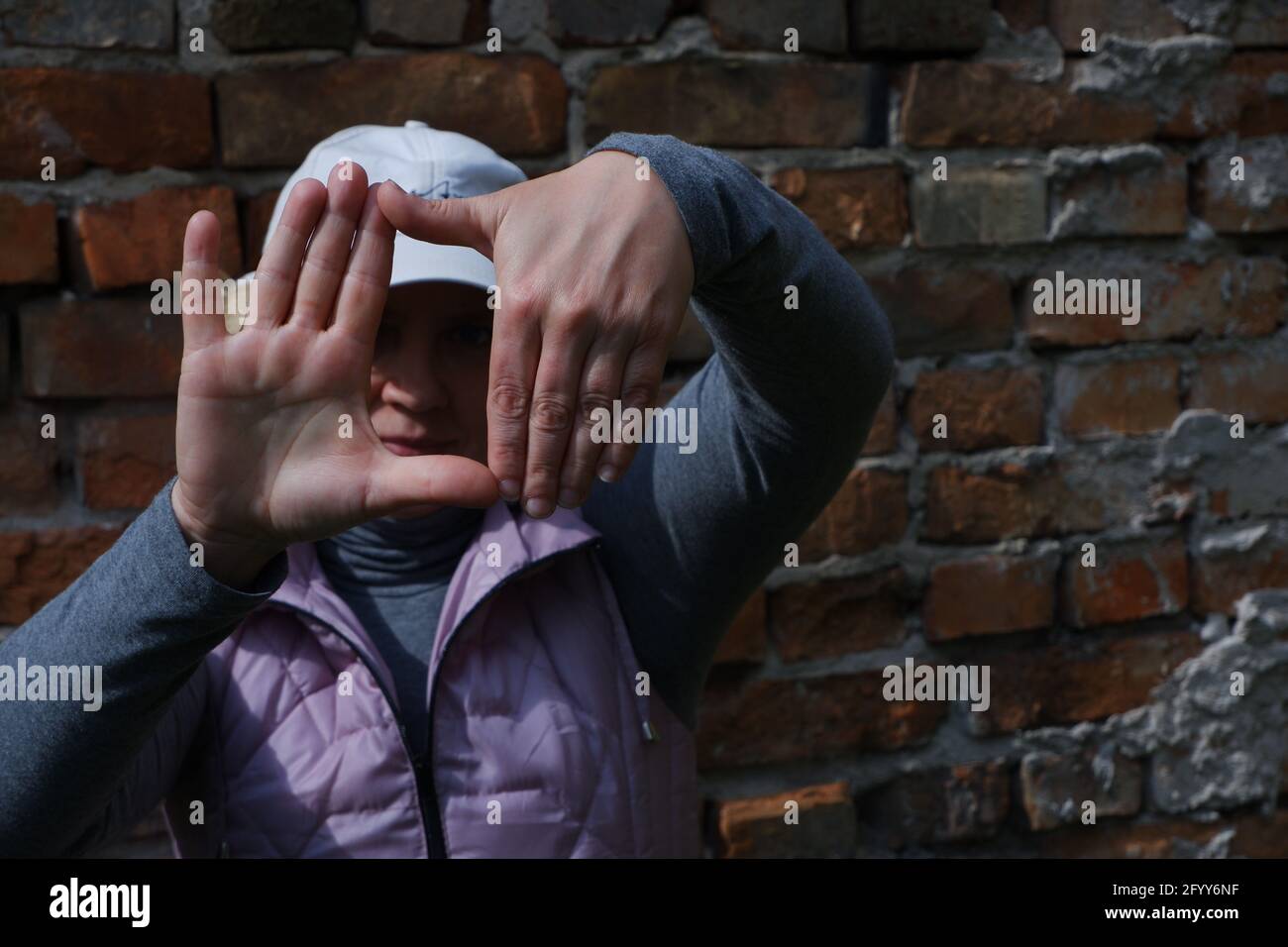 A girl near a brick wall with her hands imagines a camera. St. Veronica's Day Photographer's Day . Stock Photo
