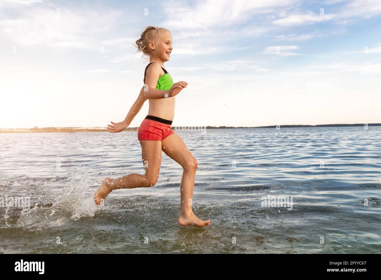 Cute adorable sporty caucasian blond school girl enjoy having fun running  water by lake or sea sand beach splashing against blue sky on summer day  Stock Photo - Alamy