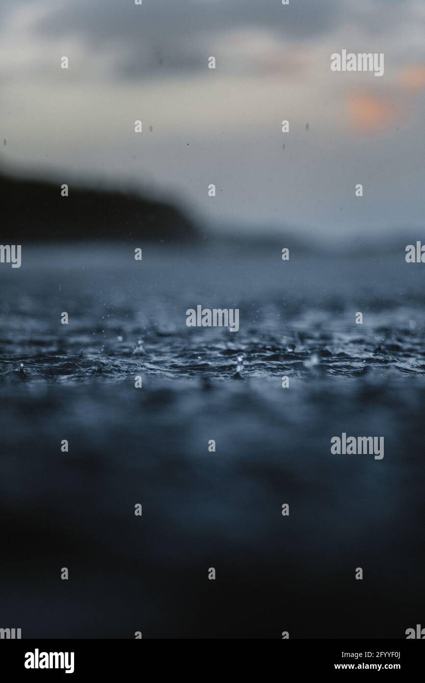 Scenic view of wavy ocean against mountain under cloudy sky at sunset on blurred background Stock Photo