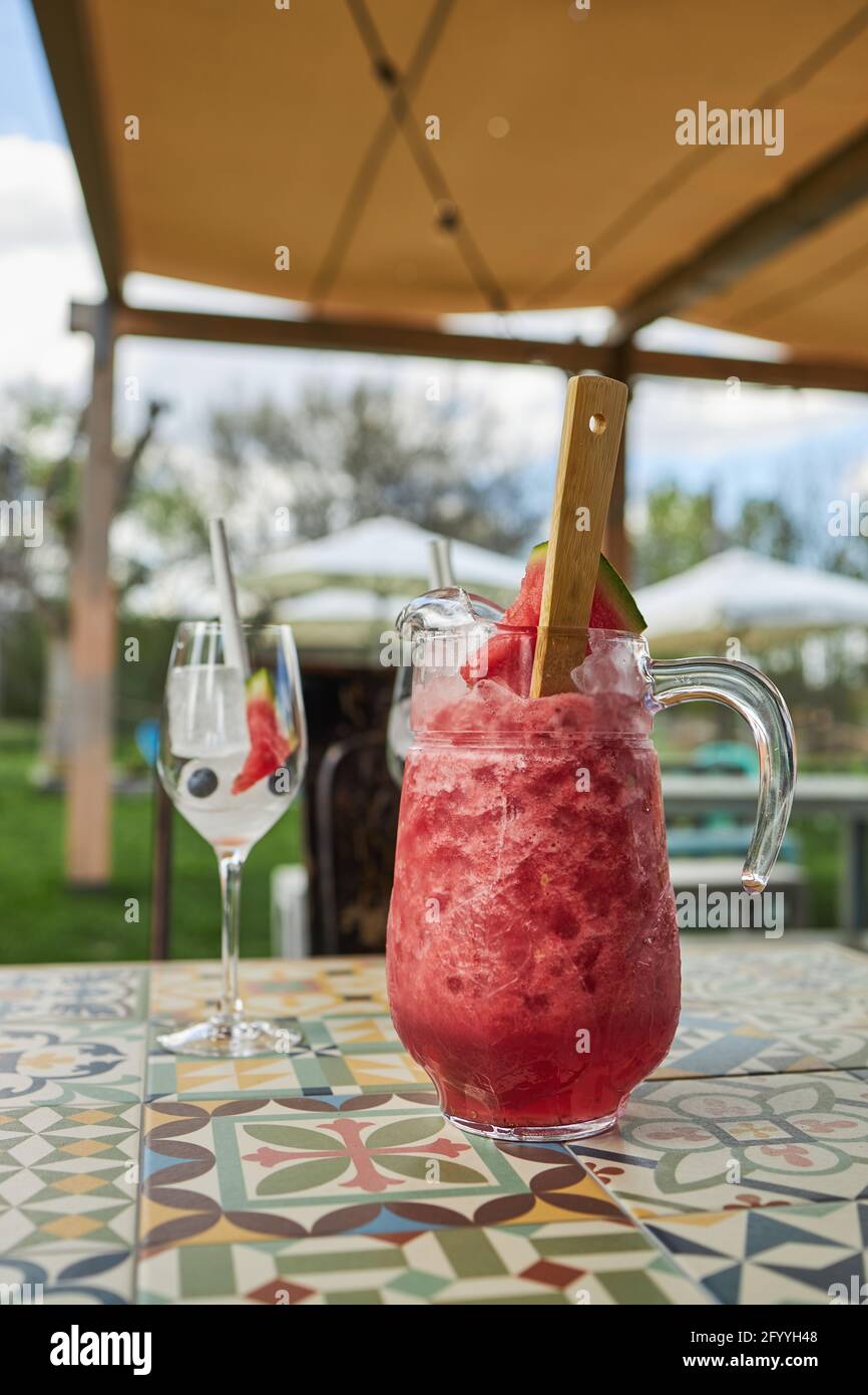Glass jug of cold watermelon gin cocktail placed near goblets with ice