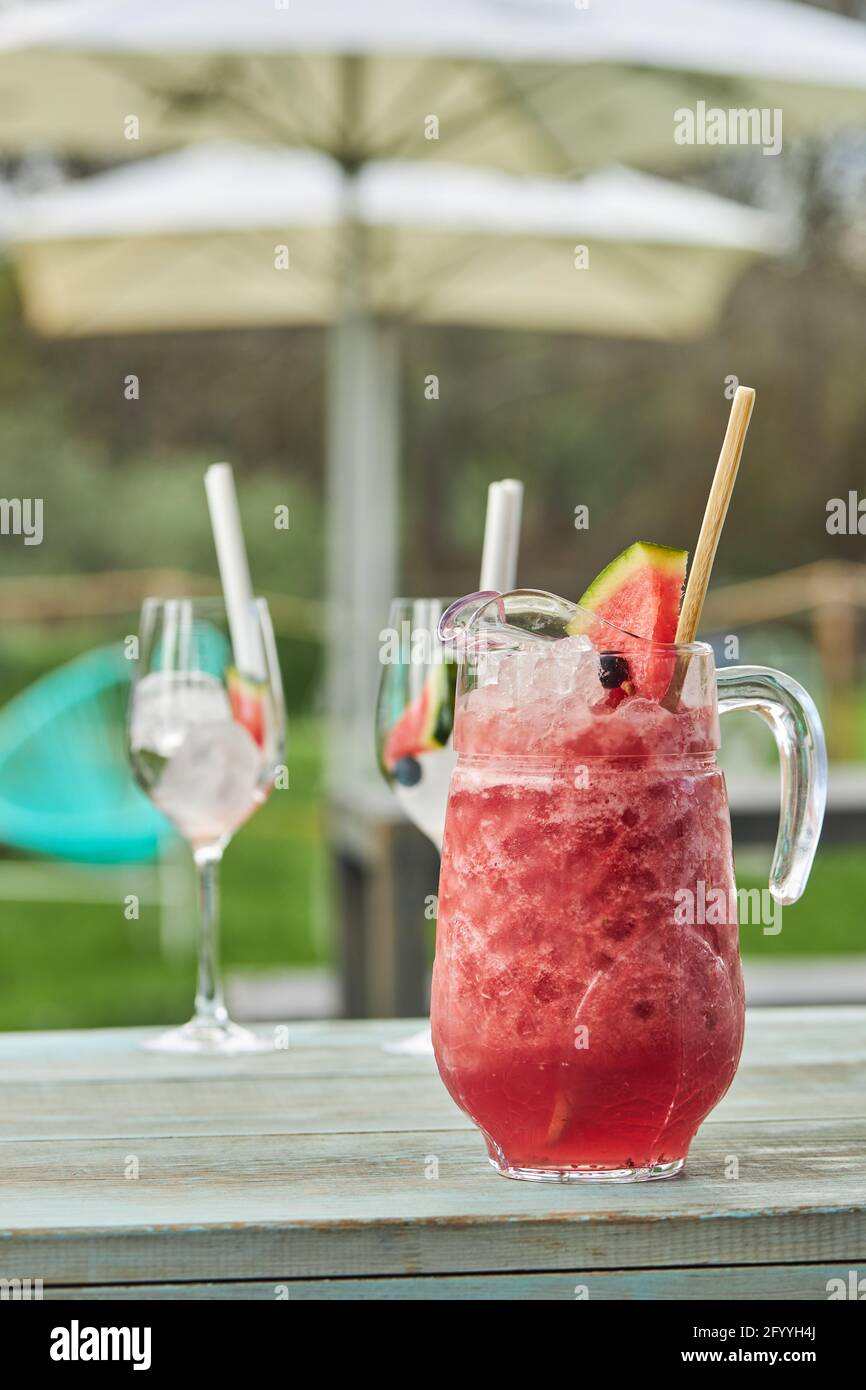 Glass jug of cold watermelon gin cocktail placed near goblets with ice
