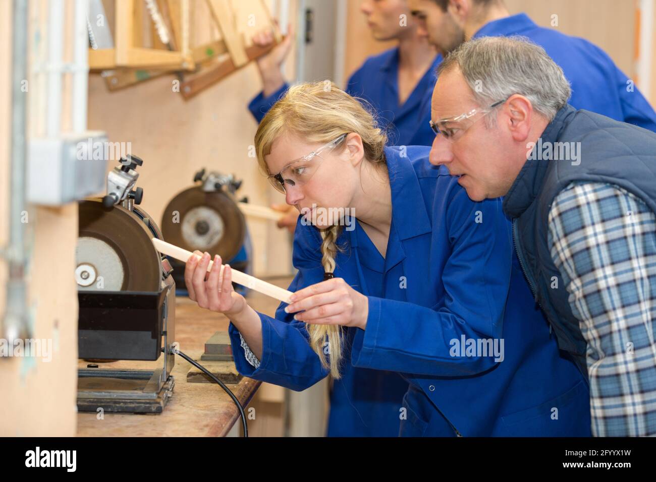 supervisor watching female apprentice carpenter use grinding wheel Stock Photo