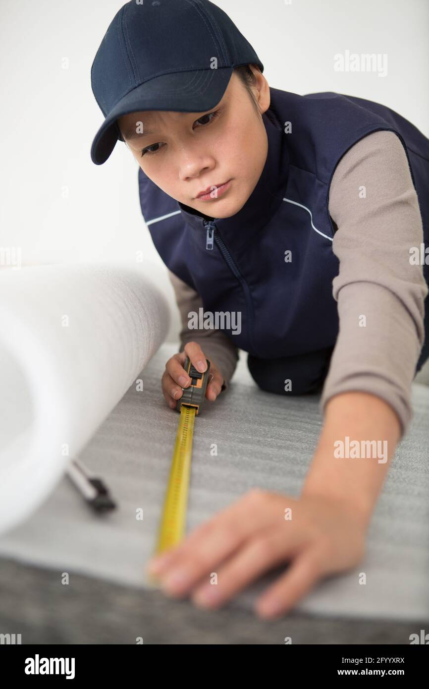 young woman in work overalls holding a tensioned tape measure Stock Photo