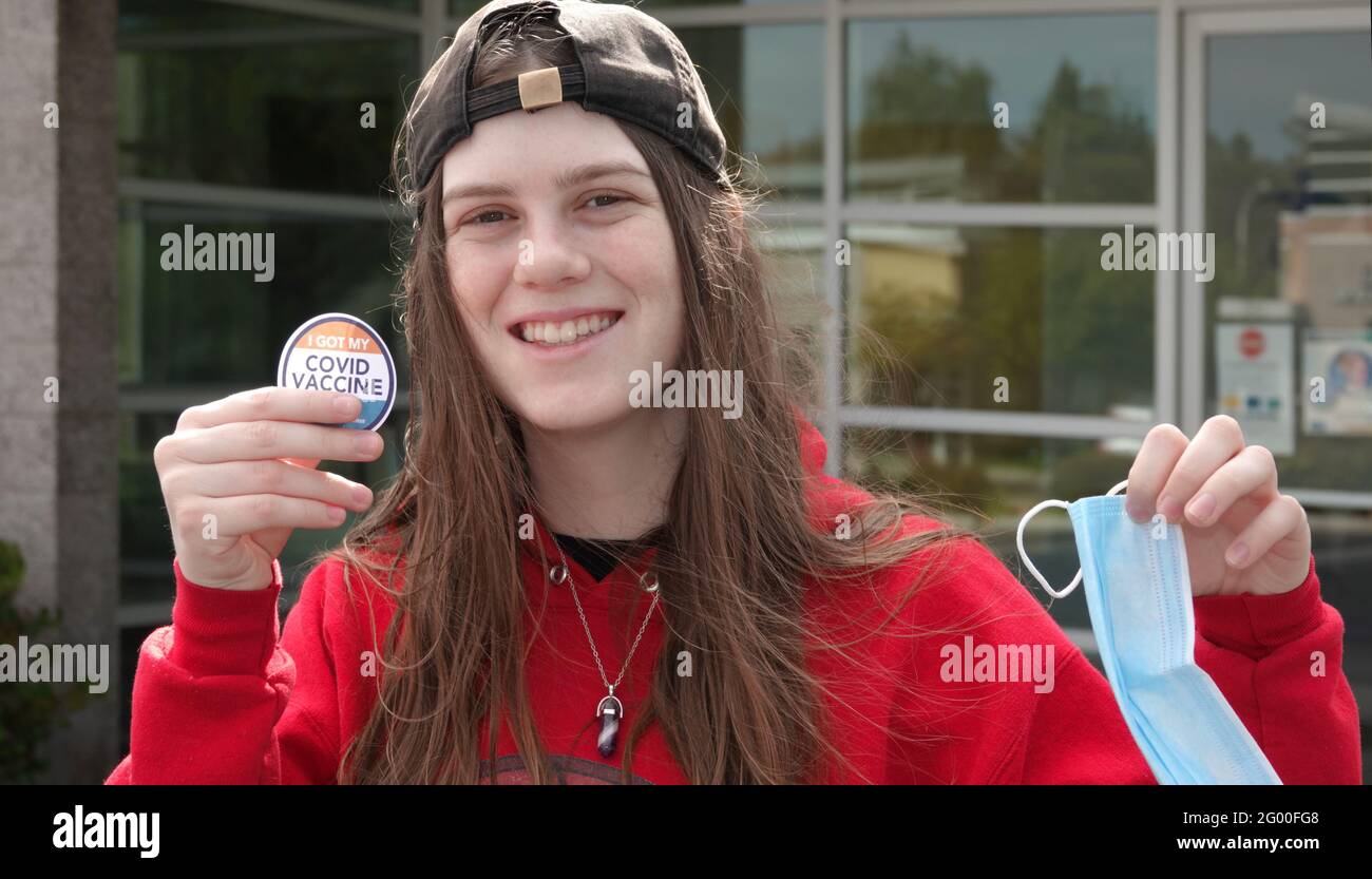 Concept image of the pandemic coming to an end: A  happy teenager shows off her vaccination sticker and discards her face mask. Stock Photo