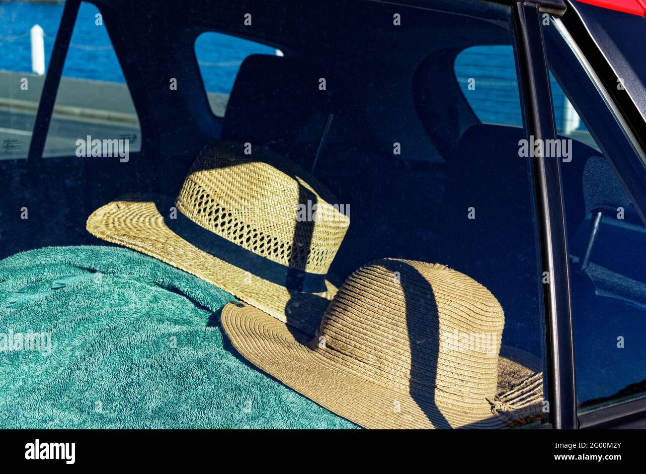 Two straw sun hats rest on a green towel in the back of a car - Summertime Stock Photo