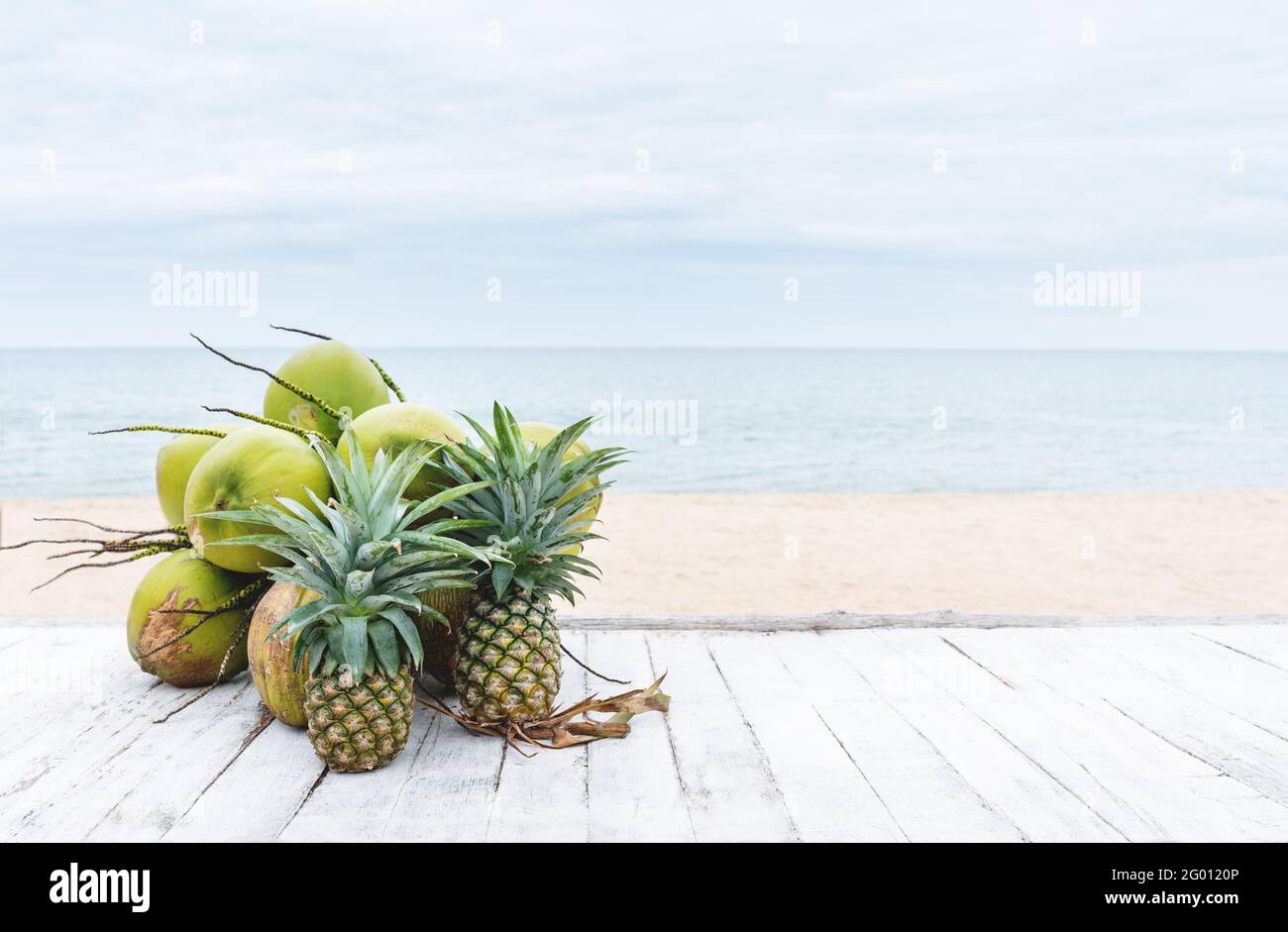 Summer background, coconuts and pineapples on white wood table, on the beach in summer Stock Photo