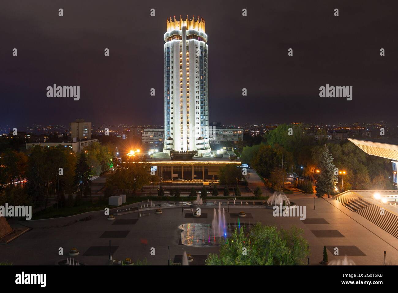 Kazakhstan Hotel tower in Abai Square, Almaty at night. Vegetation and water fountains in Abay Square in front of the Palace of the Republic. Stock Photo