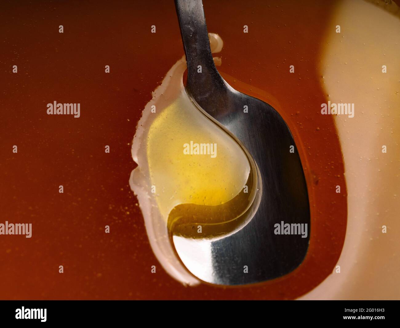 Metal spoon on surface of honey. Honey flows into the spoon. Close-up