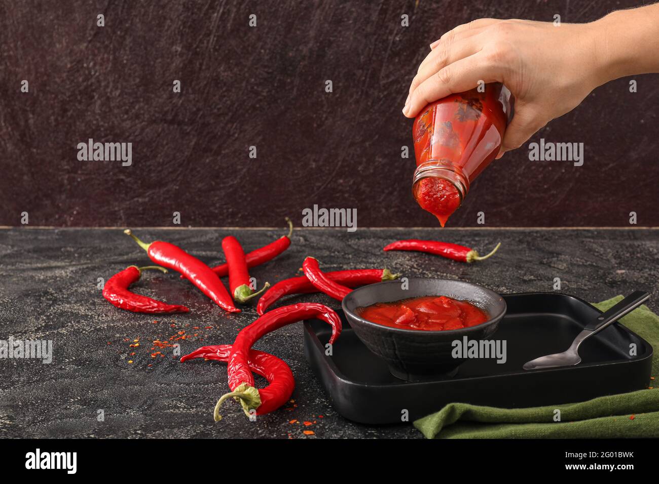 Woman pouring chili sauce from bottle in bowl on dark background Stock ...