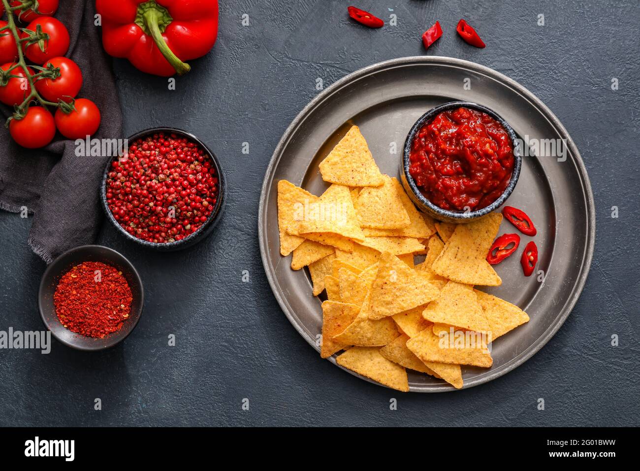 Composition with tasty chili sauce, ingredients and nachos on dark background Stock Photo