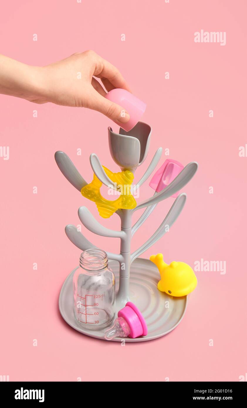 Female hand and drying rack for baby bottles on color background Stock