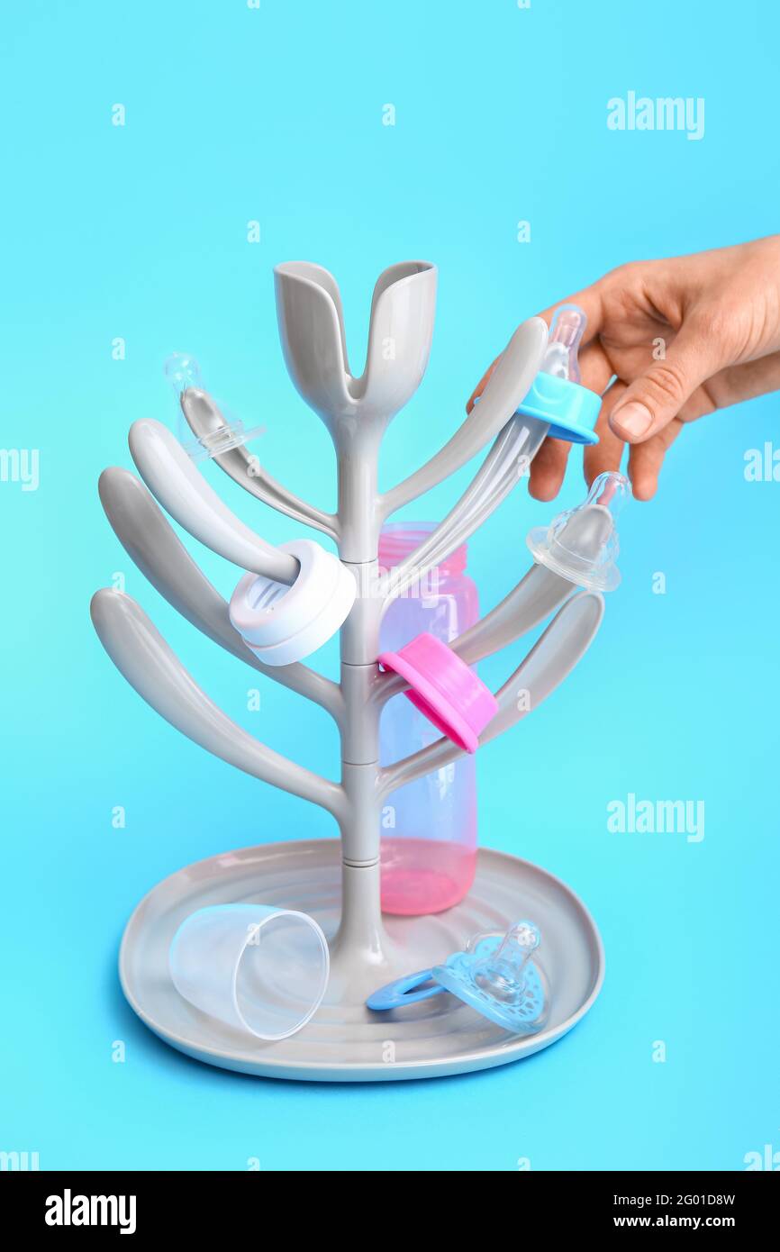 Female hand and drying rack for baby bottles on color background Stock