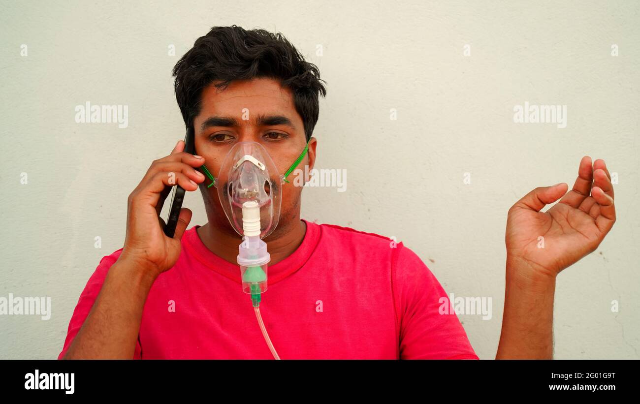 Young man infected with Covid 19 disease. Patient inhaling oxygen wearing mask and calling on mobile phone. liquid Oxygen flow in Rajasthan, India. Stock Photo