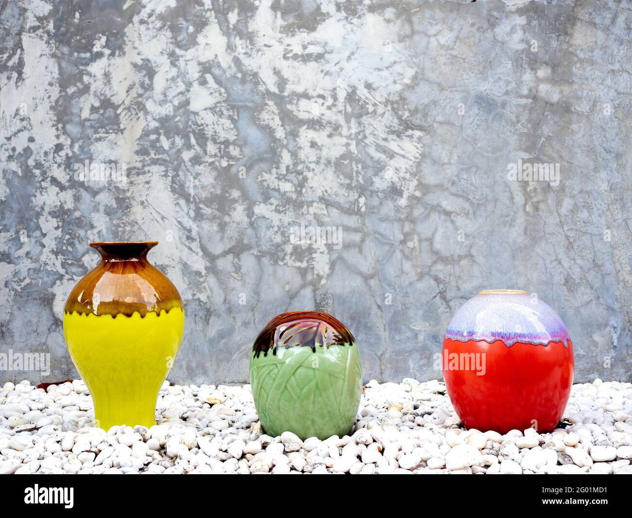 Empty various sizes and shapes of colorful ceramic vases decoration on white gravel piles on grunge concrete wall background with copy space. Stock Photo