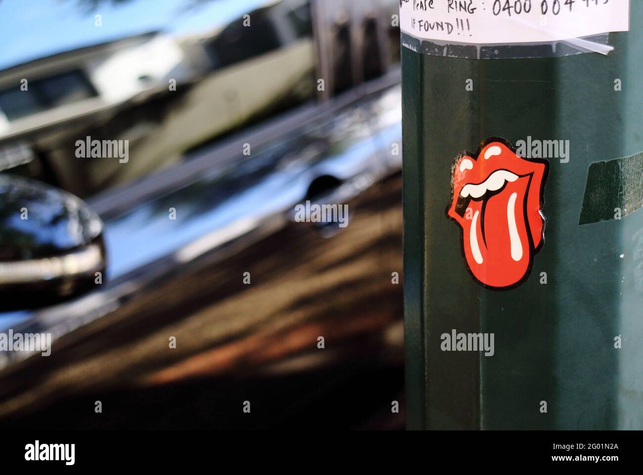 Rolling Stones Tongue and Lip logo sticker designed by John Pasche attached to a lamp pole with a car passing by in Brisbane Australia. Stock Photo