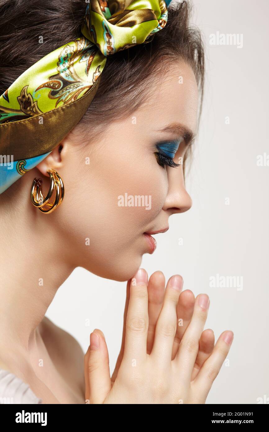 Portrait of young woman with eyes closed Female posing in headscarf with hand near face. Makeup with blue eyeshadow and yellow eyeliner. Stock Photo