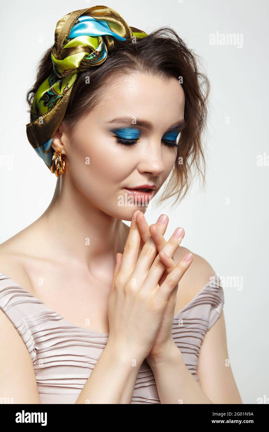 Portrait of young woman with eyes closed Female posing in headscarf with hand near face. Makeup with blue eyeshadow and yellow eyeliner. Stock Photo