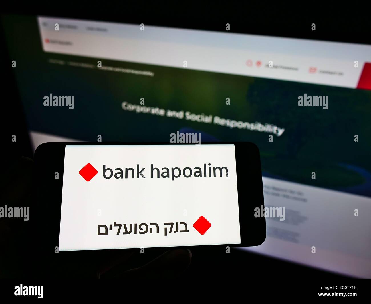 Person holding mobile phone with logo of Israeli financial company Bank Hapoalim B.M. on screen in front of web page. Focus on phone display. Stock Photo
