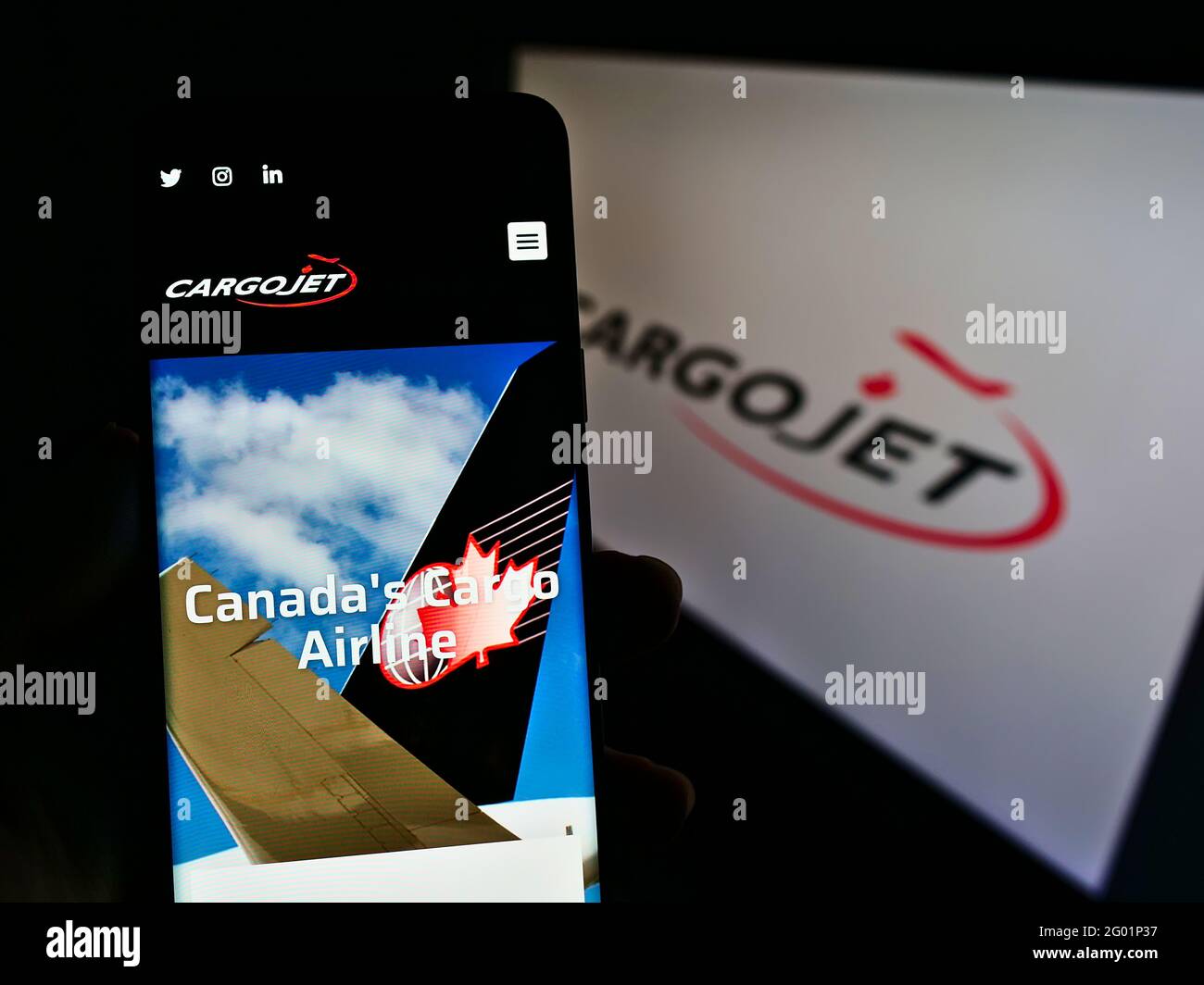 Person holding smartphone with website of Canadian cargo airline Cargojet Inc. on screen in front of company logo. Focus on center of phone display. Stock Photo