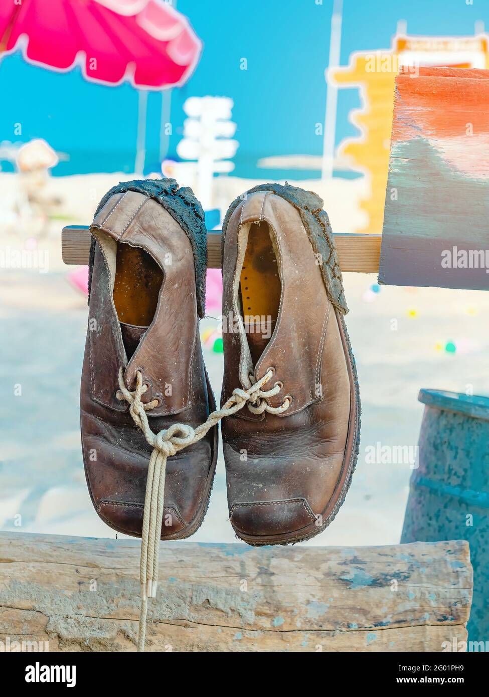 Pair of old brown leather shoes tied together with shoelaces hanging at the  old vintage wooden pole at the sandy beach. Used leather boots shoes at th  Stock Photo - Alamy