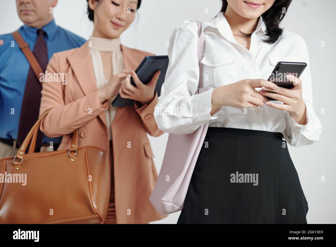Cropped image of business people standing in queue and using mobile applications on smartphones Stock Photo