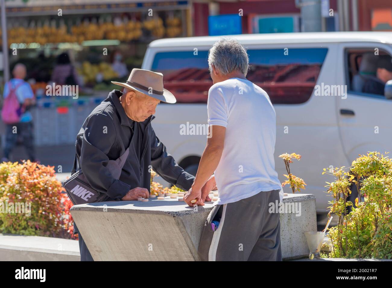 A large concrete anti-terrorist vehicle barrier doubles as a mahjong table for two men in the Sydney suburb of Cabramatta New South Wales, Australia Stock Photo